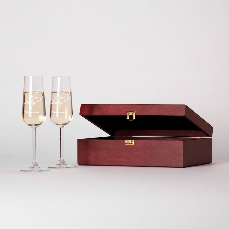 May include: Two engraved champagne flutes in a mahogany wooden box. The flutes are etched with the words "Mama & Papa" and a heart.