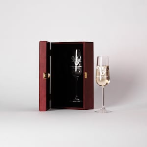 May include: A wooden box with a hinged lid is open, revealing a champagne flute inside. The flute is engraved with the text "Williams" and "Sophia & James 20.08.2021".