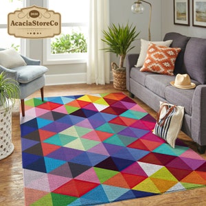May include: A colorful geometric area rug with a pattern of triangles in shades of red, blue, green, yellow, pink, and purple. The rug is laid out on a hardwood floor in a living room setting.