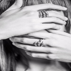 May include: Two silver rings on a person's hand. One ring is a claw design and the other is a stack of three bands.