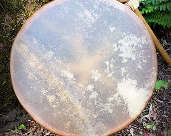 May include: A brown leather drum with a natural wood frame and a beige beater. The drum is sitting on a bed of brown leaves and moss.