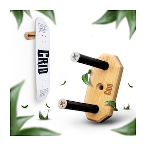 Könnte beinhalten: Eine Skateboard-Wandhalterung aus Holz mit zwei schwarzen Metallarmen. Die Halterung ist aus hellem braunem Holz gefertigt und hat den Schriftzug "GRID" eingraviert. Die Halterung ist für zwei Skateboards ausgelegt.