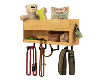 May include: A bamboo pet organizer with a shelf and hooks. The shelf holds a plush bear, a green bone-shaped toy, and a bag of dog food. Below, there are several leashes and a dog waste bag. The organizer is mounted on a white wall.