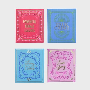 Puede incluir: Cuatro tarjetas decorativas cuadradas con diseños de libros. Las tarjetas son de color rosa, azul y morado con letras doradas. El texto de las tarjetas dice: "Powerful Female Leaders", "True Crime", "Fairy Tales" y "Love Story".