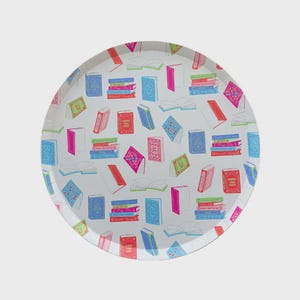 May include: A round white serving tray with a colorful book pattern. The tray features illustrations of open and closed books in various colors, including pink, blue, green, and red. The books are scattered across the tray's surface.