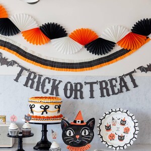 Halloween-themed party setup with Trick or Treat banner and other decorations, cake, and treats on a table.