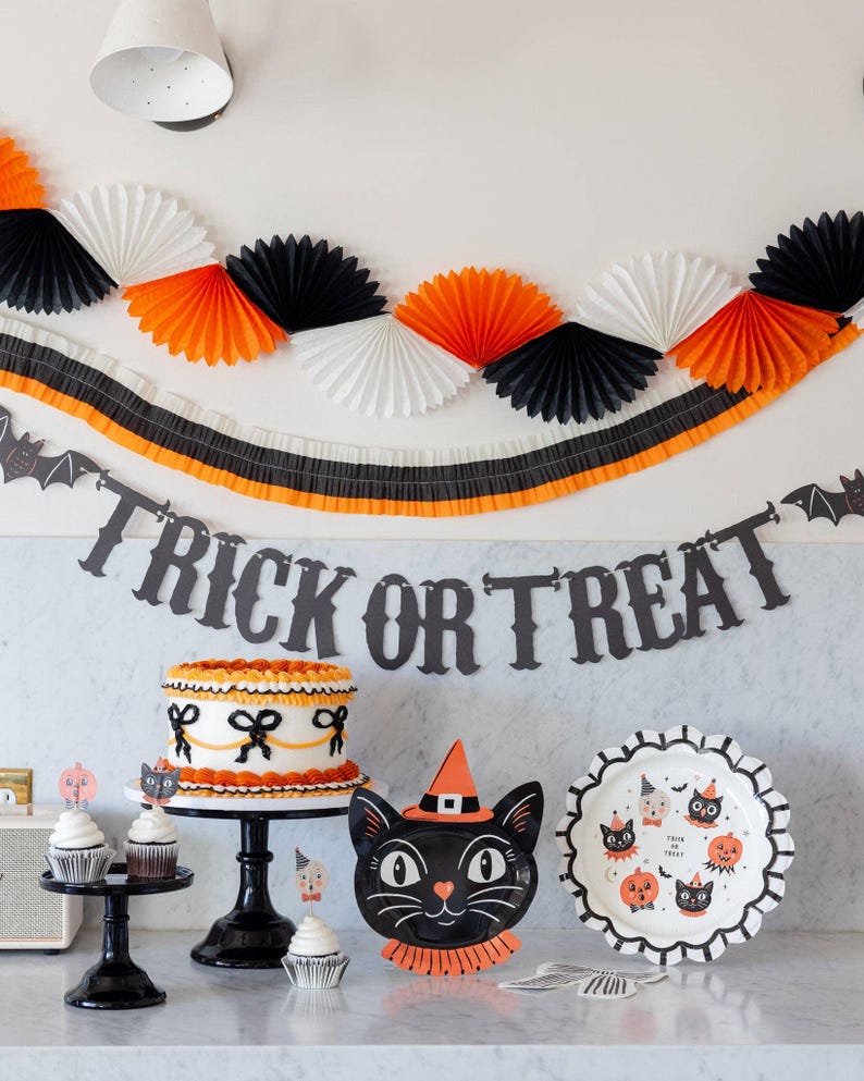 Halloween-themed party setup with Trick or Treat banner and other decorations, cake, and treats on a table.