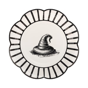 May include: A round scalloped plate with a white center and a black and white striped border. The center of the plate features a detailed black and white illustration of a pointed hat with a wide brim, rendered in a sketch-like artistic style.