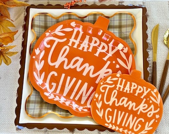May include: Two orange pumpkin-shaped paper plates with scalloped edges. The plates have a white design with the text "Happy Thanks Giving" on each plate.