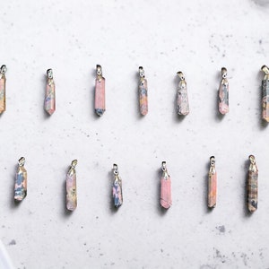 May include: Twelve pink and white crystal pendants with silver accents. The pendants are arranged in two rows of six on a white surface.