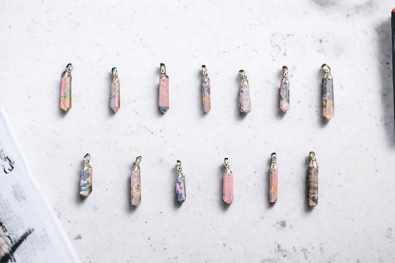May include: Twelve pink and white crystal pendants with silver accents. The pendants are arranged in two rows of six on a white surface.