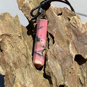May include: A pink and black crystal pendant on a black cord. The crystal is faceted and has a silver bail.