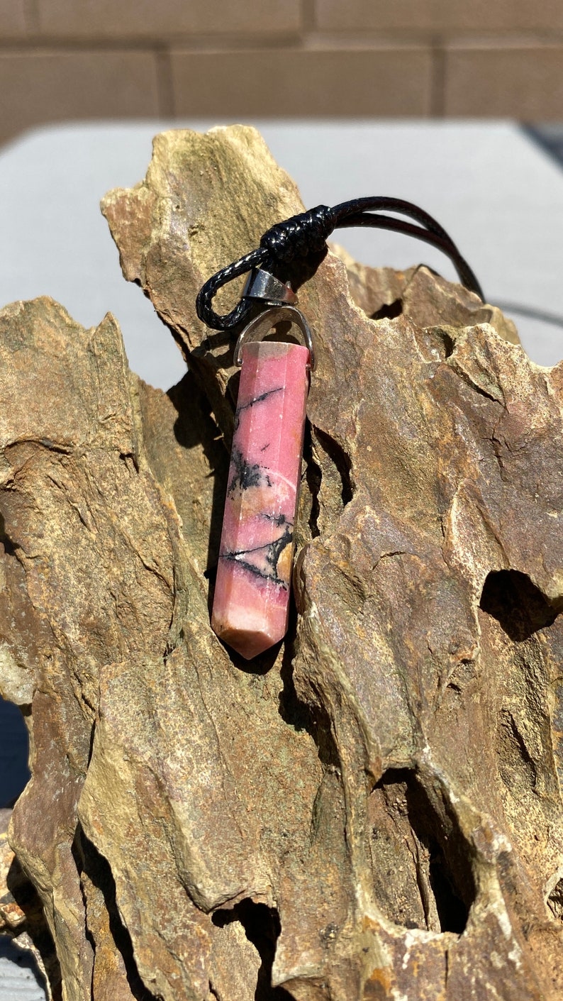 May include: A pink and black crystal pendant on a black cord. The crystal is faceted and has a silver bail.