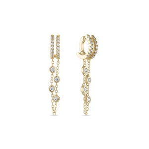 May include: A pair of gold earrings with a dangling chain and small clear stones. The earrings are designed to be worn as a single earring.