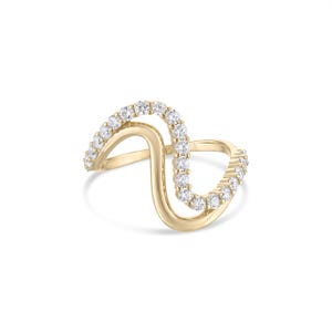 May include: A gold-colored ring with a unique, flowing design. The ring features a wave-like shape, with a line of small, clear gemstones set along the curves. The ring is set against a white background.