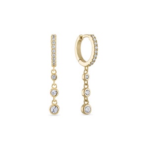 May include: Gold hoop earrings with a dangling chain of small round clear stones. The hoop is lined with small clear stones.