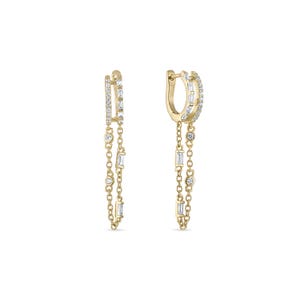 May include: A pair of gold-colored hoop earrings with dangling chains. Each earring features a hoop with embedded clear stones and a chain with a mix of round and rectangular clear stones. The earrings are set against a white background.