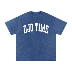 Op de afbeelding: Blauw t-shirt met de witte tekst "DJO TIME" in een boog. Het shirt heeft een ronde hals en korte mouwen. De stof heeft een licht vervaagde, vintage uitstraling.