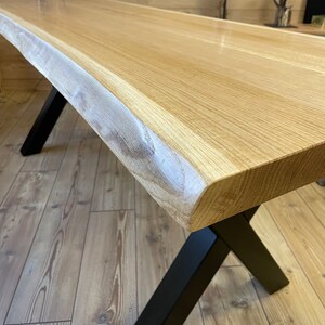 Op de afbeelding: Een houten tafel met een live edge blad en zwarte metalen X-vormige poten. De tafel is gemaakt van natuurlijk hout en heeft een rustieke uitstraling.