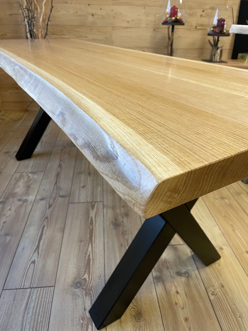 Op de afbeelding: Een houten tafel met een live edge blad en zwarte metalen X-vormige poten. De tafel is gemaakt van natuurlijk hout en heeft een rustieke uitstraling.