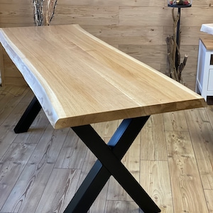 Op de afbeelding: Een grote eettafel van natuurlijk hout met een live edge blad en zwarte X-vormige poten.