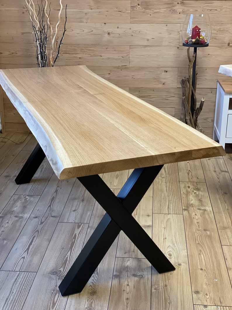 Op de afbeelding: Een grote eettafel van natuurlijk hout met een live edge blad en zwarte X-vormige poten.
