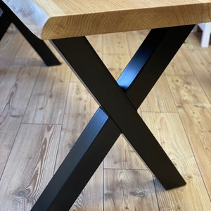 Op de afbeelding: Een houten tafelblad met een levende rand en zwarte X-vormige metalen poten.
