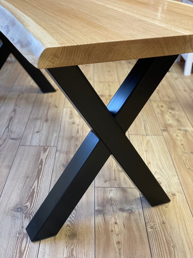 Op de afbeelding: Een houten tafelblad met een levende rand en zwarte X-vormige metalen poten.