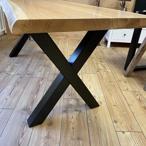 Op de afbeelding: Een houten tafelblad met een levende rand en een zwarte metalen X-vormige basis.