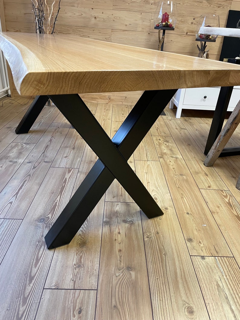 Op de afbeelding: Een houten tafelblad met een levende rand en een zwarte metalen X-vormige basis.