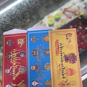May include: Three colorful envelopes with ornate designs and text. The envelopes are red, blue, and yellow. The red envelope has gold and yellow designs. The blue envelope has gold and white designs. The yellow envelope has gold and red designs.