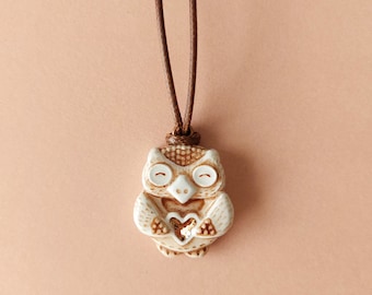 May include: A brown cord necklace with a ceramic owl pendant. The owl is white with brown accents and has a small heart in its chest.