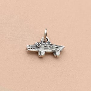 May include: Silver charm in the shape of an alligator with a textured surface.