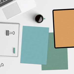May include: A white laptop computer, a spiral bound notebook, a cup of coffee, and three sheets of paper with a dotted pattern. The sheets of paper are blue, green, and orange.
