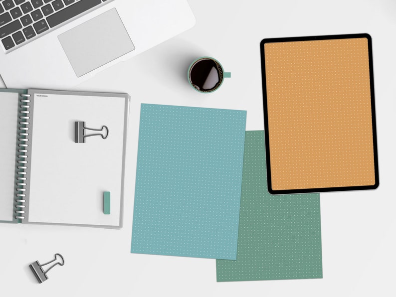 May include: A white laptop computer, a spiral bound notebook, a cup of coffee, and three sheets of paper with a dotted pattern. The sheets of paper are blue, green, and orange.