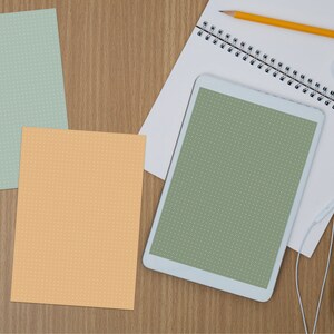 May include: A white tablet computer with a green screen, a spiral bound notebook, a pencil, a white mouse, and white earbuds on a wooden surface.
