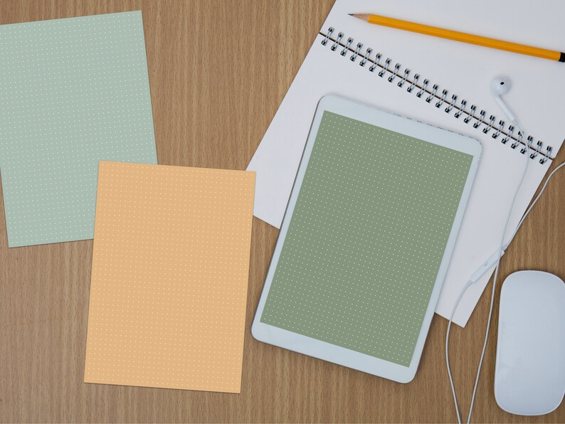 May include: A white tablet computer with a green screen, a spiral bound notebook, a pencil, a white mouse, and white earbuds on a wooden surface.