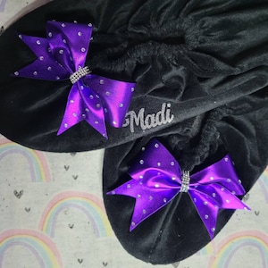 Può includere: Due scrunchies in velluto nero con fiocchi di raso viola adornati con strass argentati. Lo scrunchie a sinistra ha il nome "Madi" ricamato.