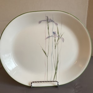 Puede incluir: Plato de servir ovalado blanco con un borde verde y un diseño floral de iris púrpuras sobre un fondo blanco.