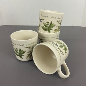 May include: Four white ceramic mugs with a green and white floral design and the text "Chamomile, Basil, Sage, Mint, Lavender" printed around the rim.