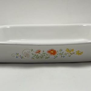 Puede incluir: Fuente rectangular blanca para hornear con bordes redondeados. El plato presenta un diseño floral con flores naranjas, amarillas y azules. El diseño está en el lateral. Un clásico de la cocina.