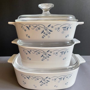 Peut inclure: Un ensemble de trois plats à gratin en verre blanc avec des motifs floraux bleus. Les plats sont empilés les uns sur les autres, le plus grand en bas et le plus petit en haut. Les plats ont des couvercles.