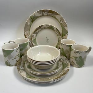 May include: A set of white ceramic dinnerware with a green and brown leafy pattern. The set includes four bowls, four mugs, and four dinner plates.