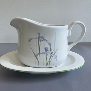 Puede incluir: Salsera de cerámica blanca con borde verde y diseño floral de iris morados. La salsera está sobre un plato a juego.