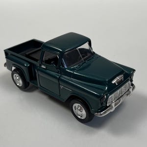 Puede incluir: Modelo fundido a presión de color verde oscuro de una camioneta clásica. El camión presenta una parrilla cromada detallada, ruedas plateadas y una caja negra. El modelo es un vehículo de estilo vintage.