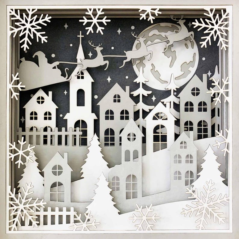 May include: A white papercraft scene depicting a winter village with houses, trees, and a full moon. Santa Claus is flying in his sleigh pulled by reindeer in the sky above the village.