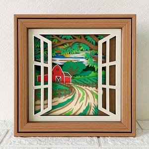 May include: A framed paper art piece depicting a rural landscape viewed through an open window. The scene includes a red barn, a winding dirt road, and green fields, all layered to create depth. The frame is made of wood.