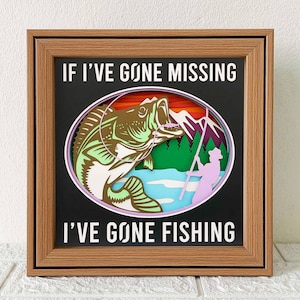 May include: A wooden framed shadow box with a paper cut-out design of a fish, a fisherman, and a lake scene. The text "If I've gone missing I've gone fishing" is printed on the black background.