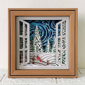 以下が含まれることがあります： 窓から見える冬の風景を描いた3Dペーパーアート作品。雪景色、松の木2本、フェンスにとまっている赤い鳥が描かれている。空は金色に輝く星が散りばめられた渦巻き状の青色である。