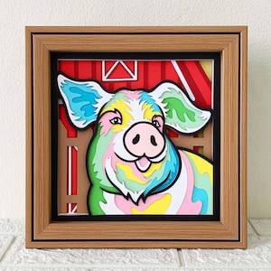 Könnte beinhalten: Ein farbenfrohes Papier-Schwein mit einer rosa Schnauze und blauen, grünen und gelben Akzenten ist in einem Holzrahmen gerahmt. Der Hintergrund ist eine rote und weiße Scheunen-Szene.